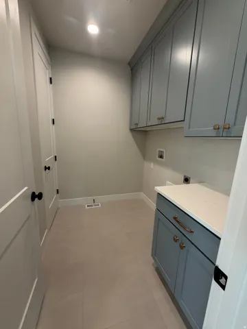 Recessed lighting illuminating a laundry area with light blue cabinetry, a white countertop, and light-toned tile flooring