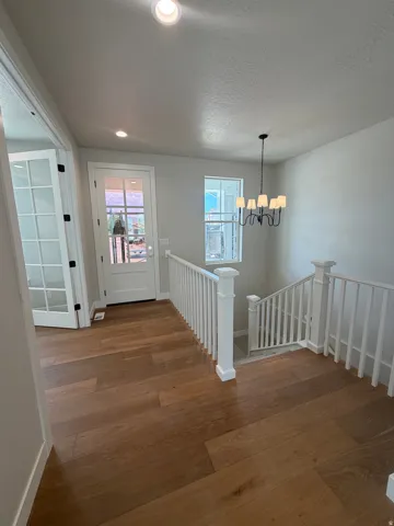 Rich wood-finish flooring, white painted railings, recessed ceiling lighting, a contemporary black chandelier, and a white paneled door with glass inserts