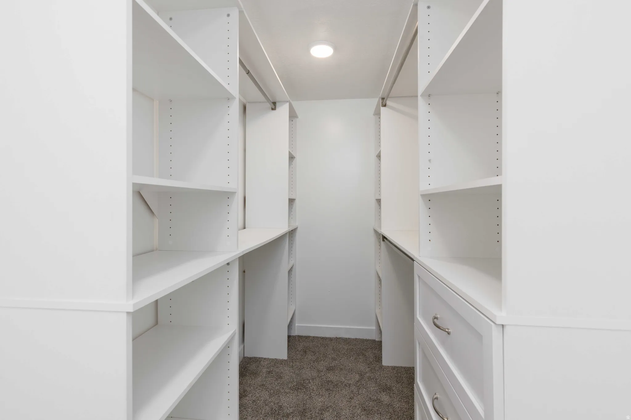 Walk-in closet with built-in white shelving, integrated drawers with metal hardware, and recessed lighting