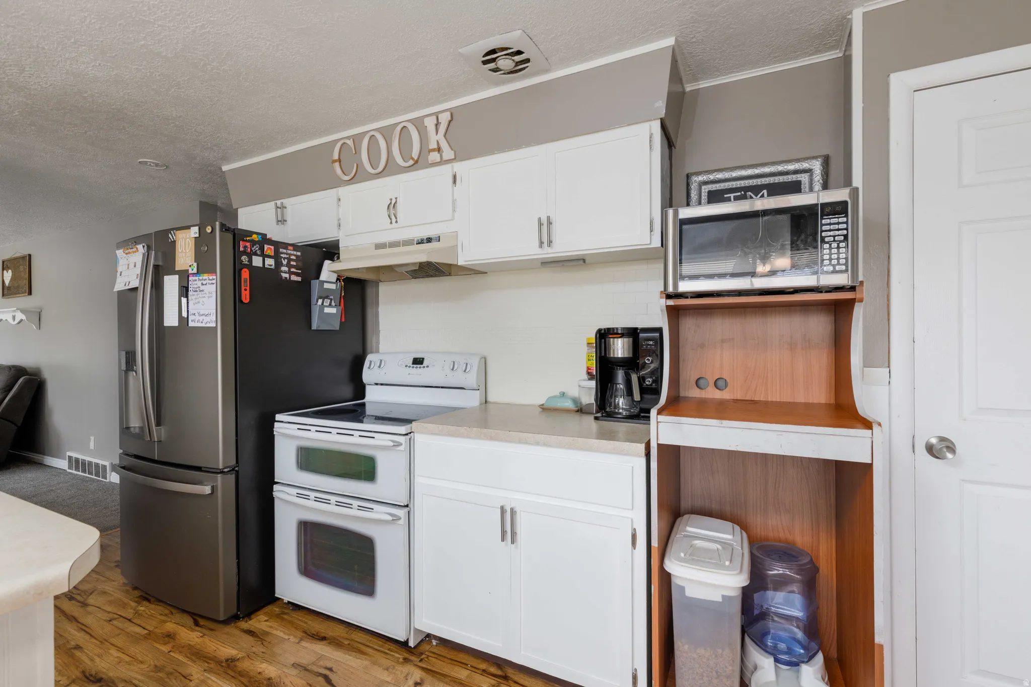 White cabinetry, light countertops, wood-finish flooring, dual wall ovens, and stainless steel refrigerator