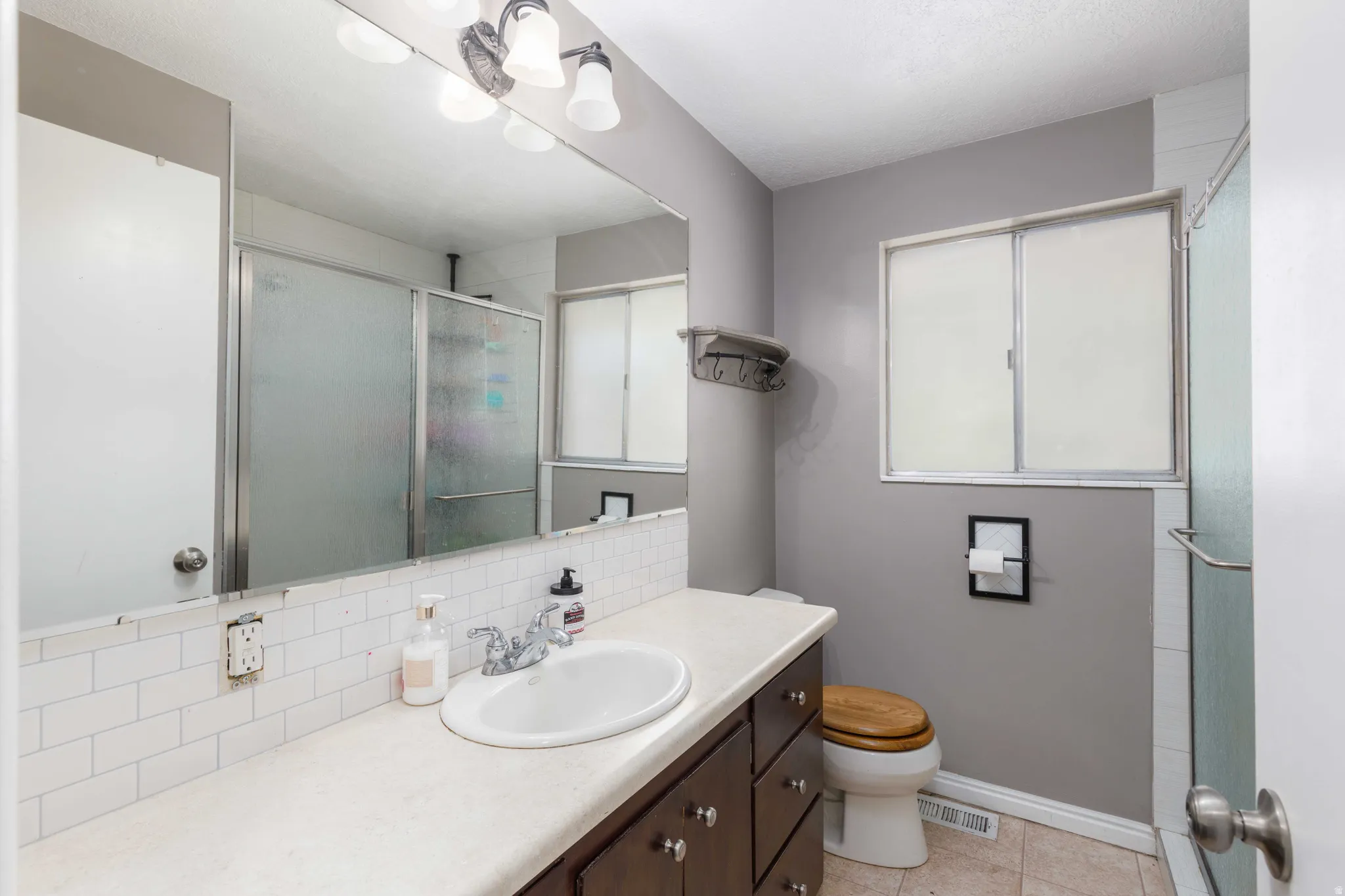 Bathroom featuring a wood-finish vanity with an integrated sink, a subway tile backsplash, a wall-mounted mirror, and a shower with a sliding glass enclosure