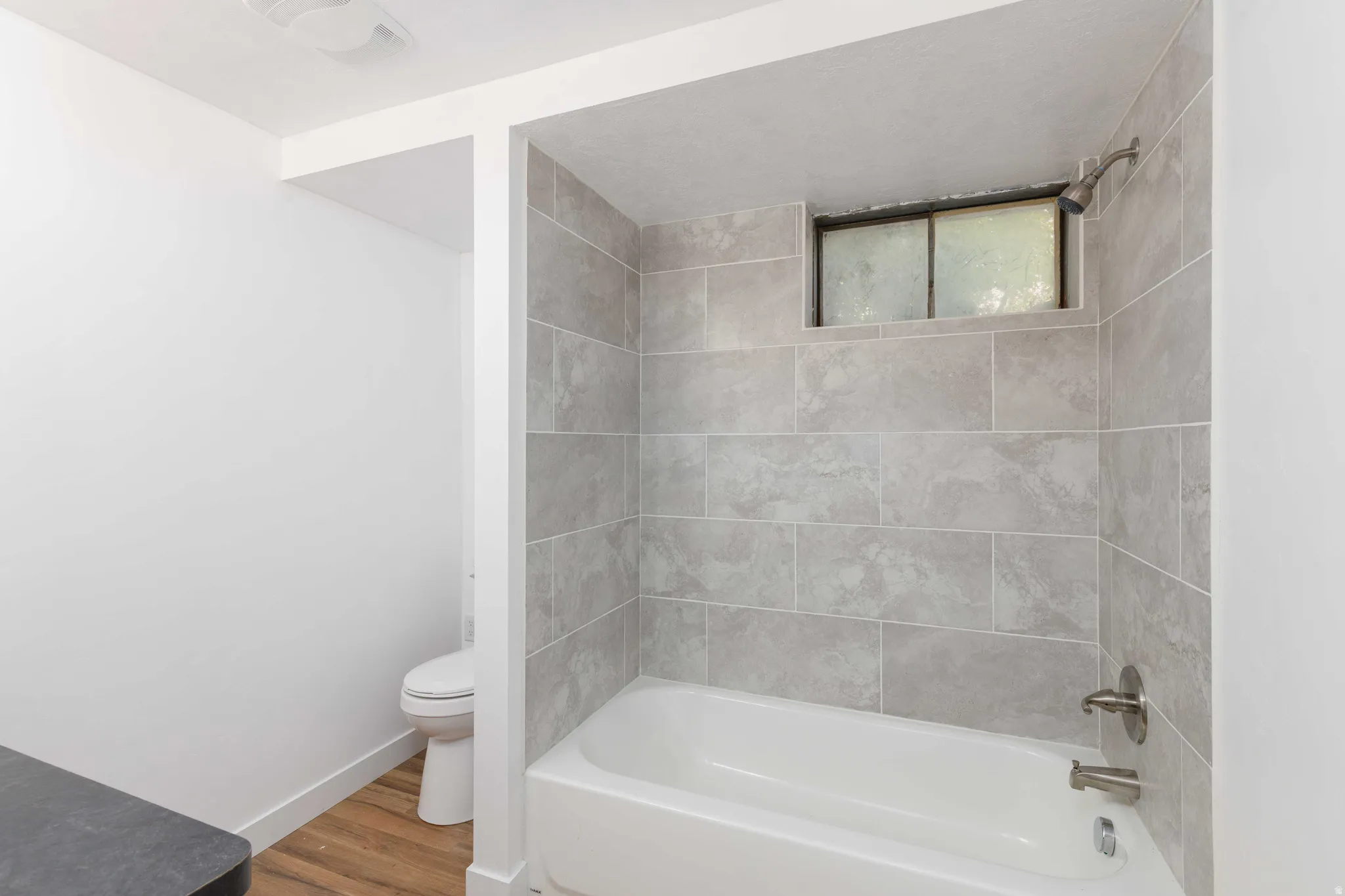 Bathtub with subway-style wall tiling and a frosted window, complemented by wood-finish flooring