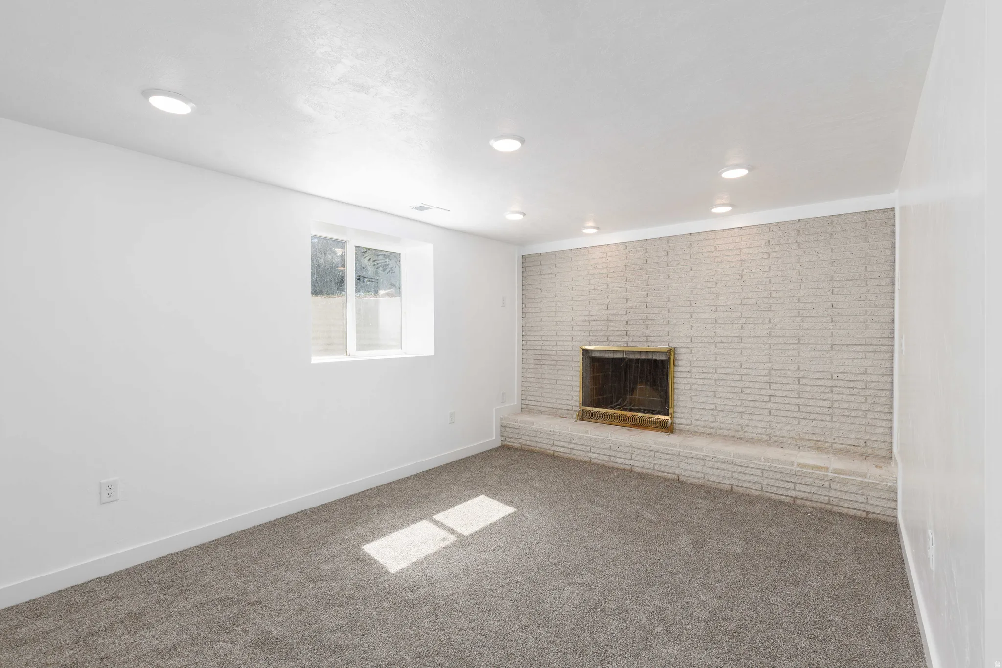 Recessed lighting, white brick fireplace with brass insert, white walls, and gray carpet flooring