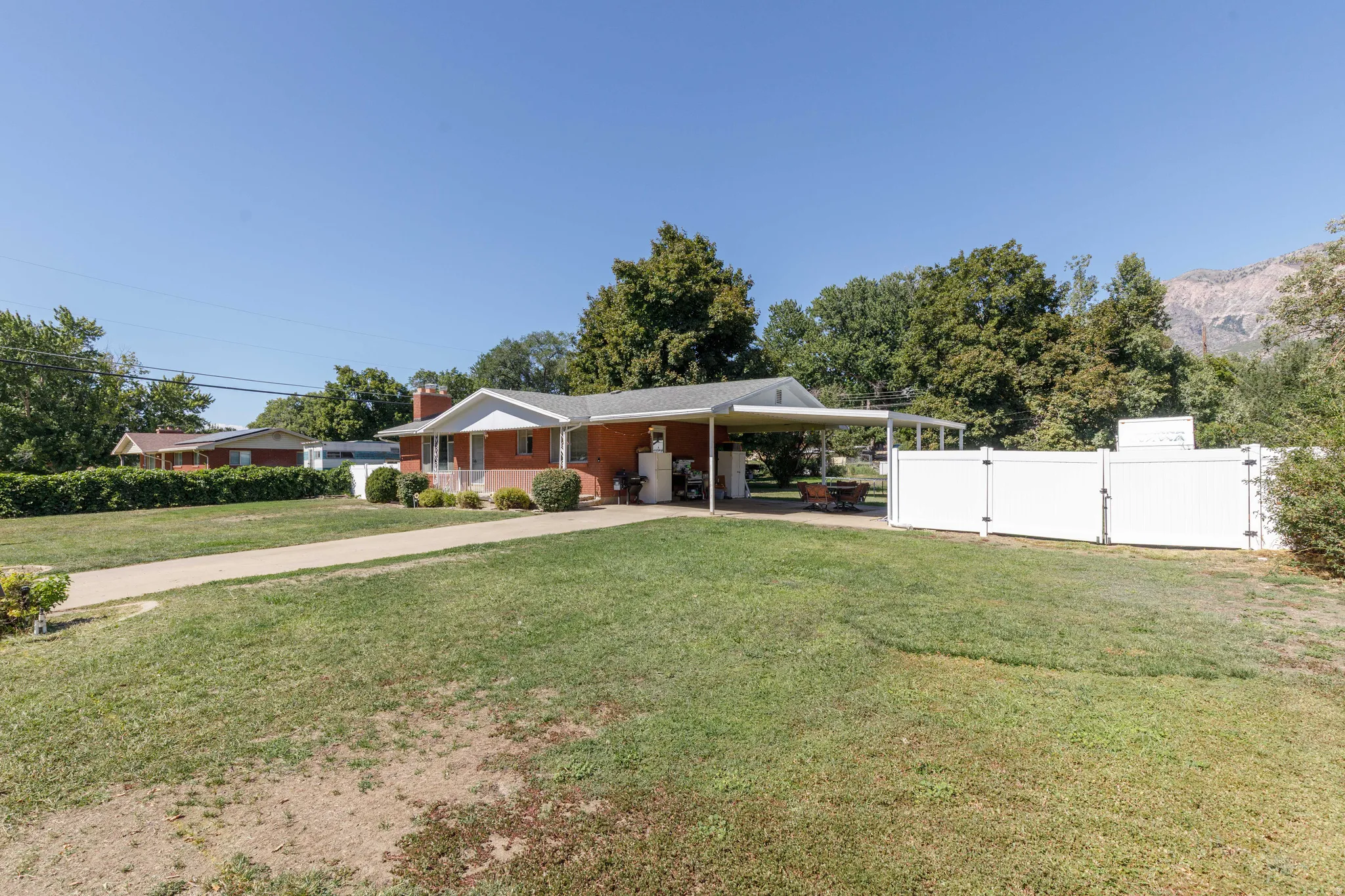 Brick exterior with white trim, covered carport, front porch, and a white privacy fence