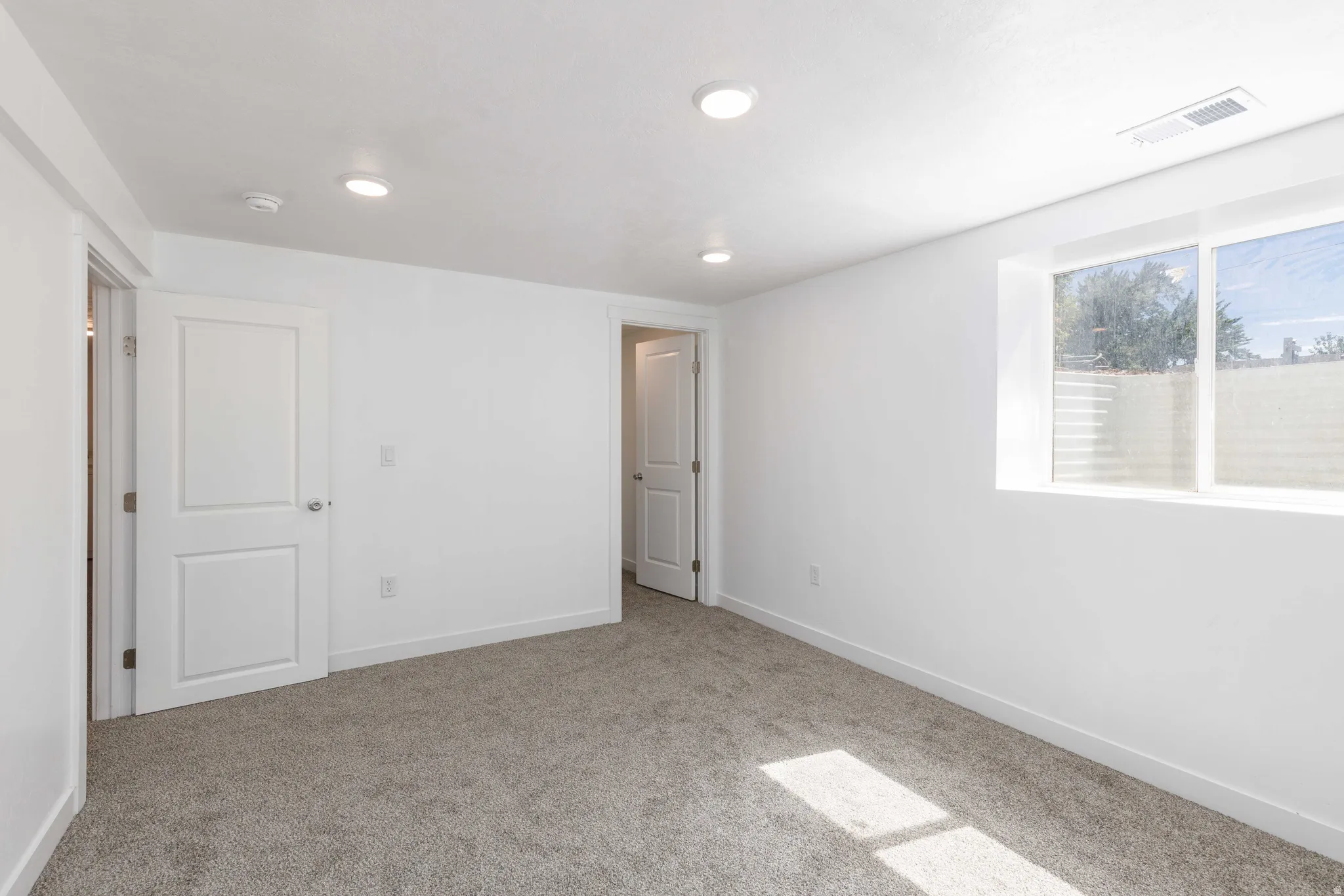 Spacious room with plush gray carpeting, recessed ceiling lighting, a large window, and crisp white trim