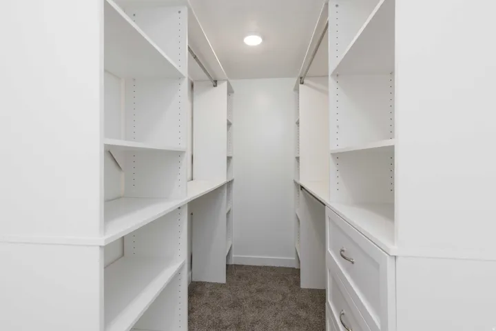 Walk-in closet with built-in white shelving, integrated drawers with metal hardware, and recessed lighting