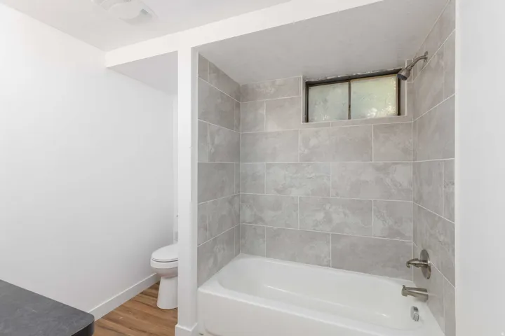 Bathtub with subway-style wall tiling and a frosted window, complemented by wood-finish flooring