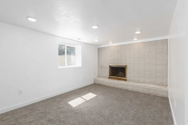 Recessed lighting, white brick fireplace with brass insert, white walls, and gray carpet flooring