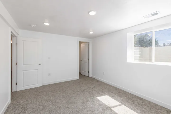 Spacious room with plush gray carpeting, recessed ceiling lighting, a large window, and crisp white trim