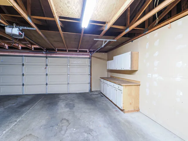 Attached garage with a sectional garage door, exposed ceiling joists, overhead lighting, built-in lower cabinetry, and upper wall-mounted cabinets