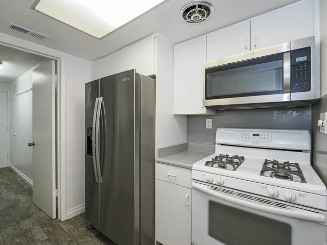 Kitchen featuring a stainless steel refrigerator, white cabinetry, a built-in microwave, a gas range, and wood-finish flooring
