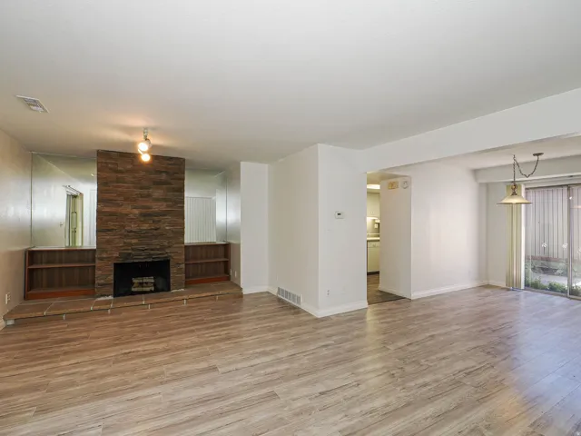 Wood-finish flooring throughout, featuring a stone-clad fireplace with built-in shelving, a kitchen pass-through, and sliding glass doors