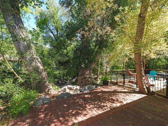 Expansive wood-finish deck with black metal railings, surrounded by mature trees and natural landscaping