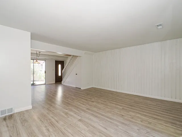 Spacious open-concept room featuring wood-finish flooring, a painted vertical plank accent wall, and a staircase with white balusters