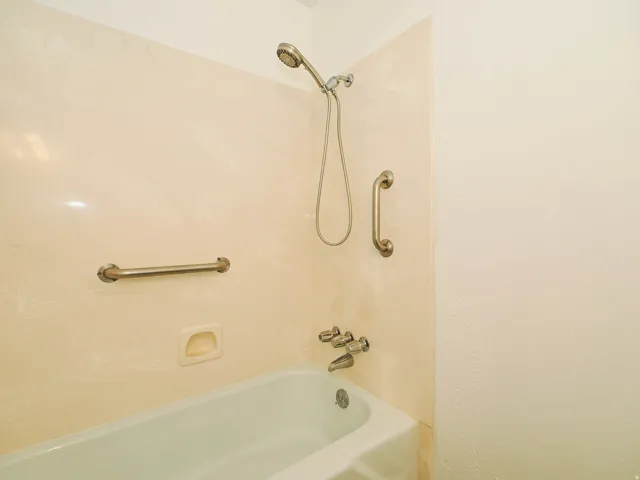 Bathtub with a handheld showerhead, wall-mounted faucet, and two grab bars