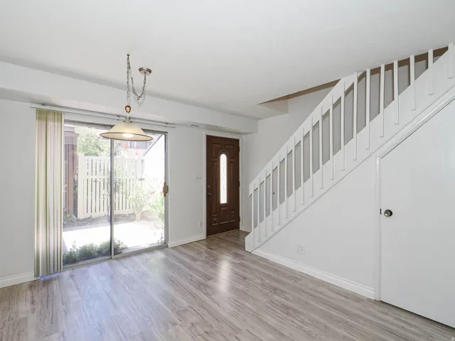 Wood-finish flooring, white staircase with balusters, sliding glass door, privacy fencing, and a built-in light fixture