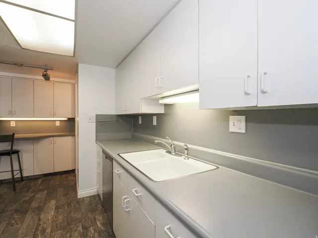 White cabinetry, light gray countertops, integrated white sink with dual faucets, wood-finish flooring, and built-in desk area