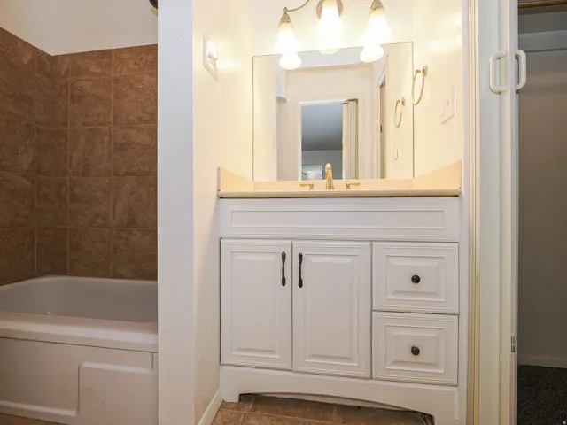 White vanity with cabinet storage and drawer storage, light-colored countertop, and a single basin sink