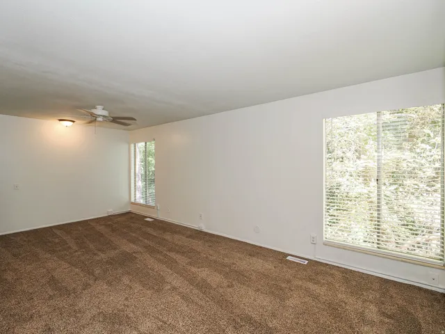 Spacious room featuring broadloom carpeting, a ceiling fan with integrated lighting, and multiple windows with horizontal blinds