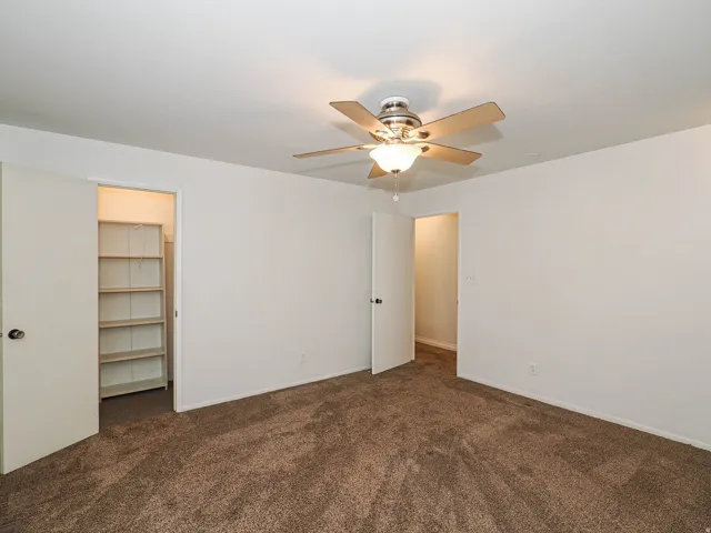 Neutral wall paint, brown carpet flooring, built-in shelving, and a ceiling fan with integrated lighting