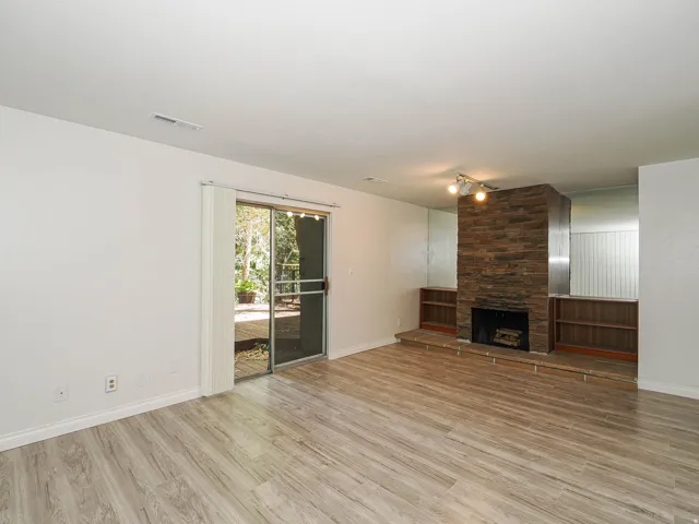 Wood-finish flooring, sliding glass door, stone-clad fireplace with hearth, track lighting, and built-in shelving