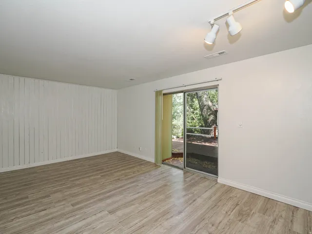 Wood-finish flooring, white paneling accent wall, track lighting, and sliding glass door