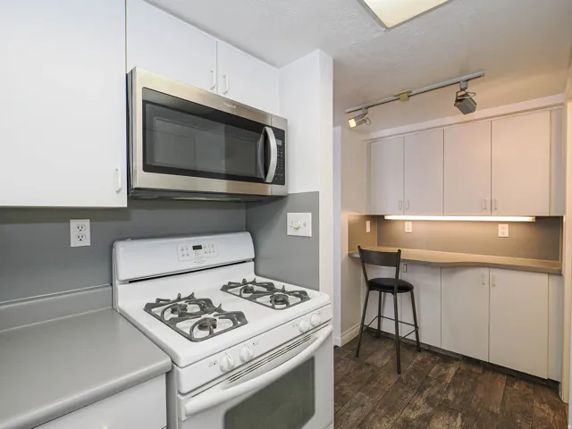 Stainless steel over-the-range microwave, white cabinetry, gray countertops, and wood-finish flooring