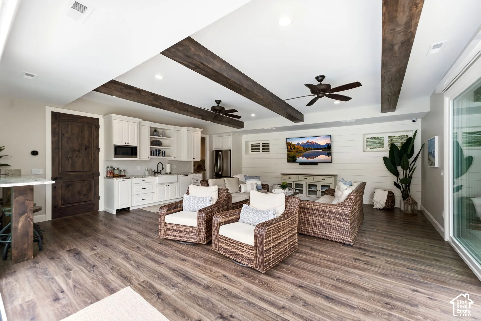 Casita- Open-concept living area with wood-finish flooring, exposed ceiling beams, recessed lighting, and a built-in kitchen area featuring white cabinetry and an apron-front sink
