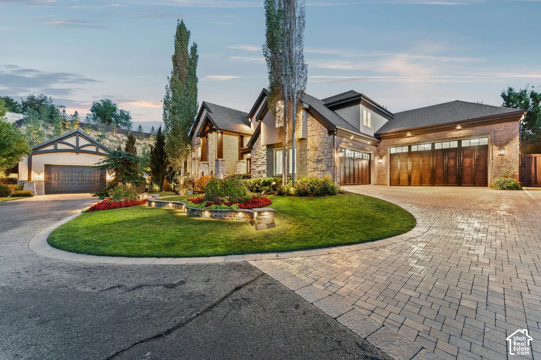 Stone facade with wood-finish garage doors, paver driveway, and landscaped circular lawn