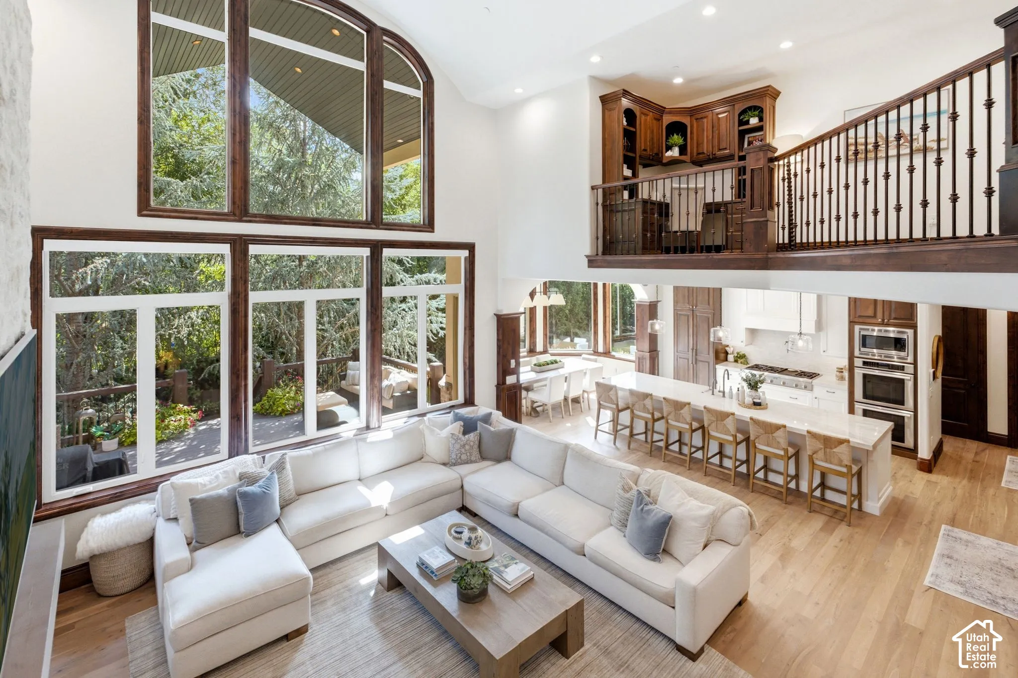 Soaring ceilings with extensive window walls, an open-concept kitchen featuring a large island, stainless steel appliances, and wood-finish flooring throughout