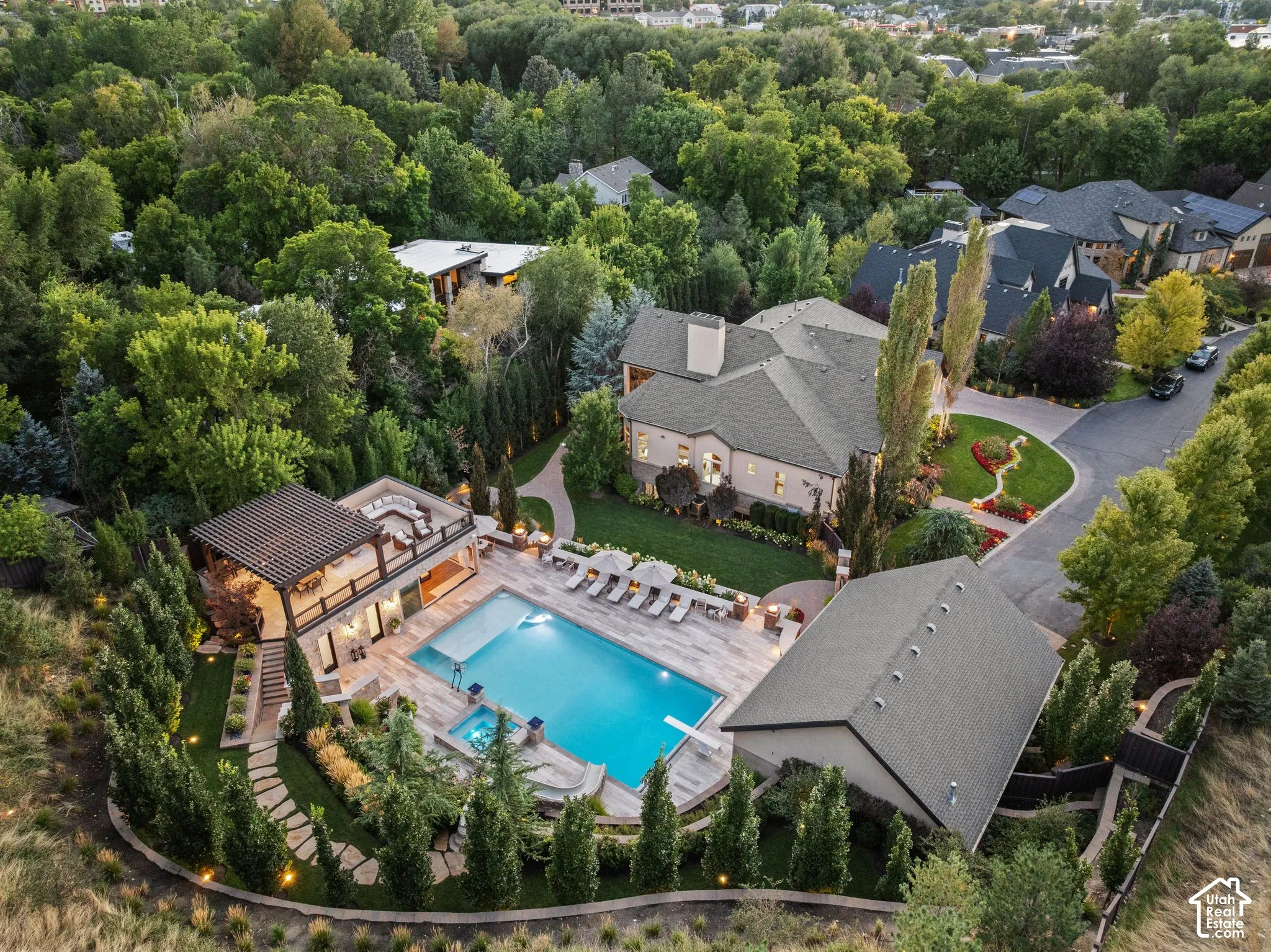 Spacious property featuring a large swimming pool, an elevated outdoor living area with a pergola, a separate outbuilding, a circular driveway, and extensive perimeter landscaping