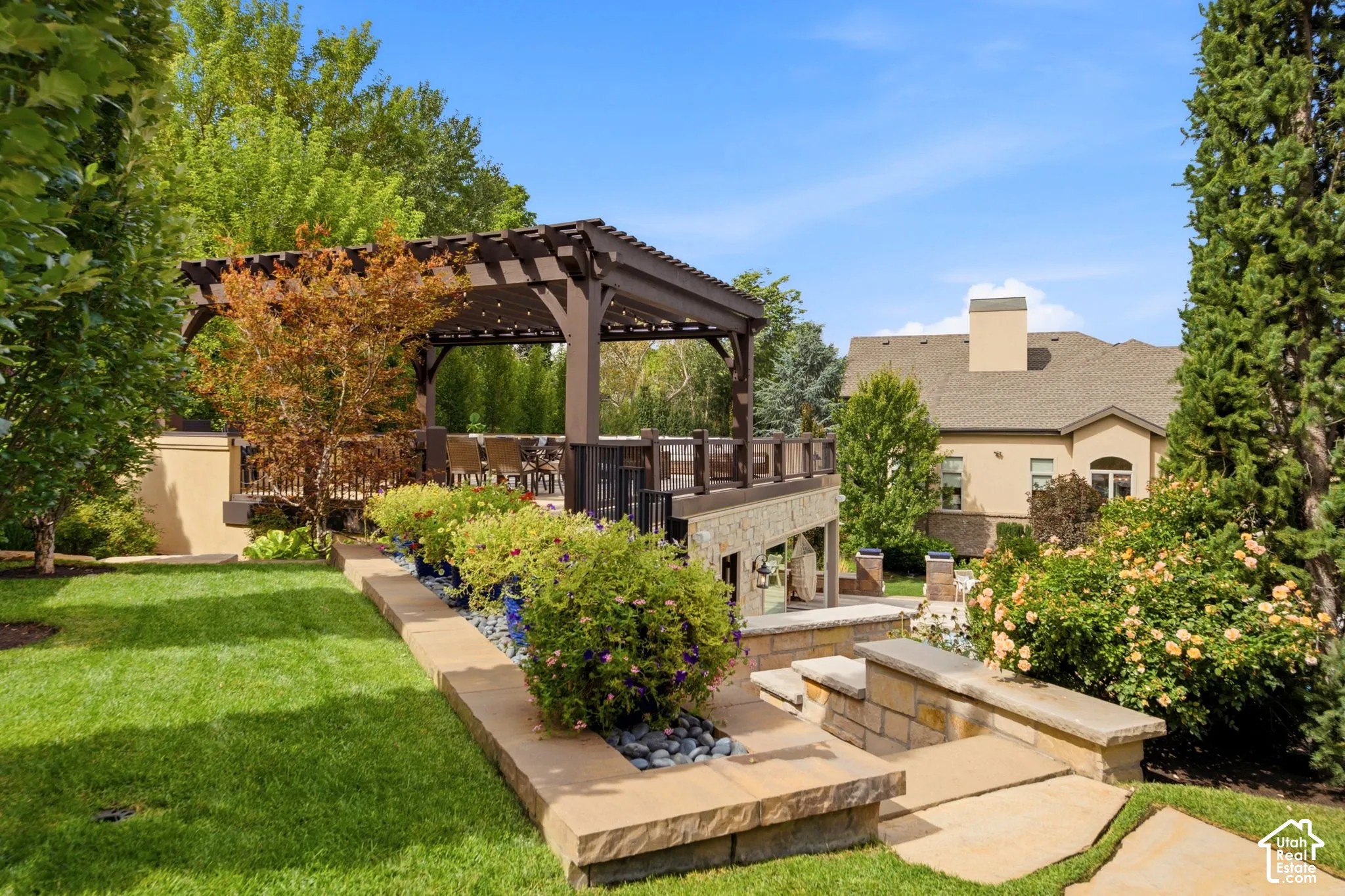 Expansive backyard featuring a manicured lawn, established landscaping, stone hardscaping, and a multi-level deck with a pergola