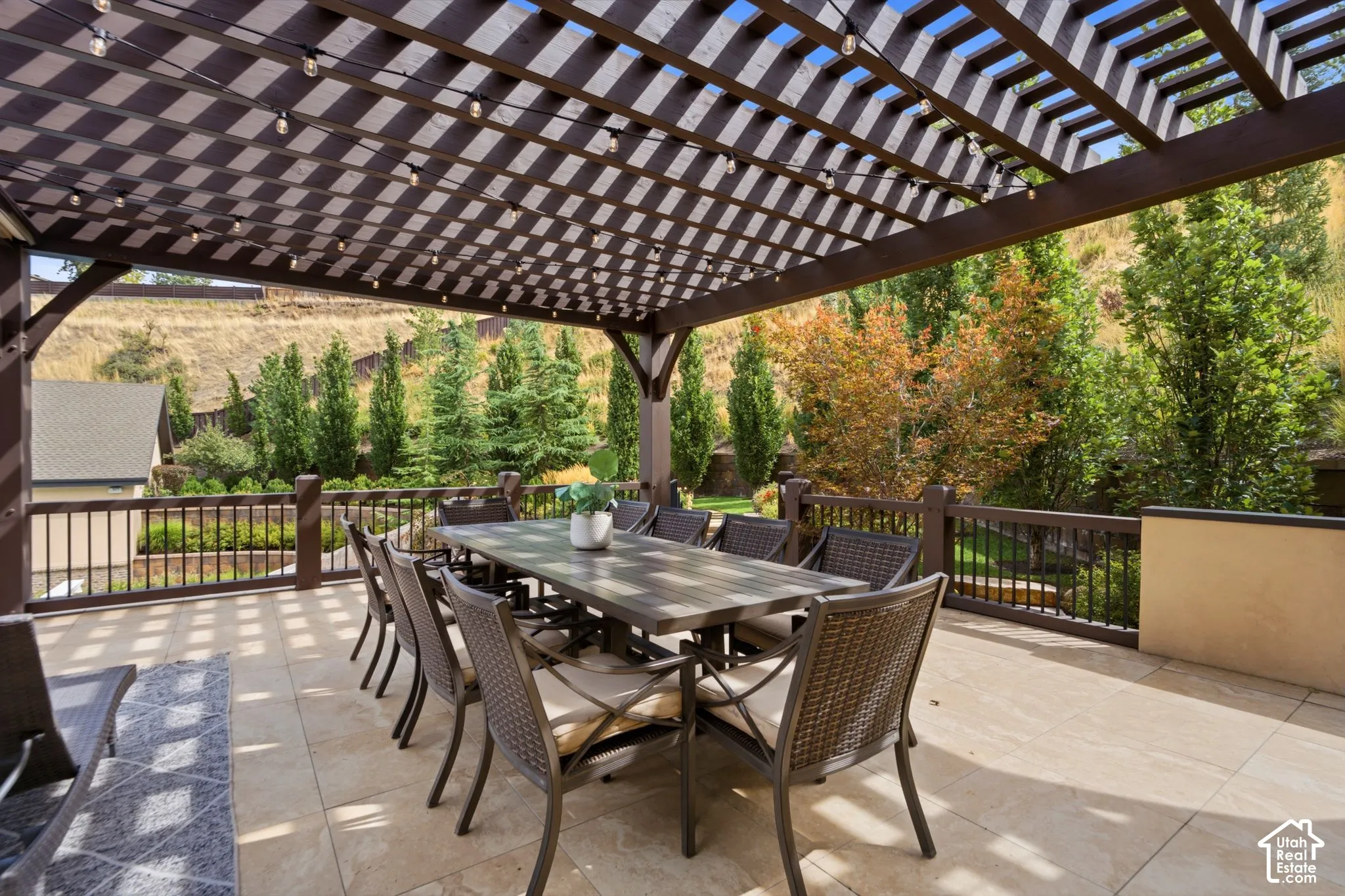 Expansive outdoor patio featuring a slatted pergola, decorative string lighting, tiled flooring, and a perimeter railing