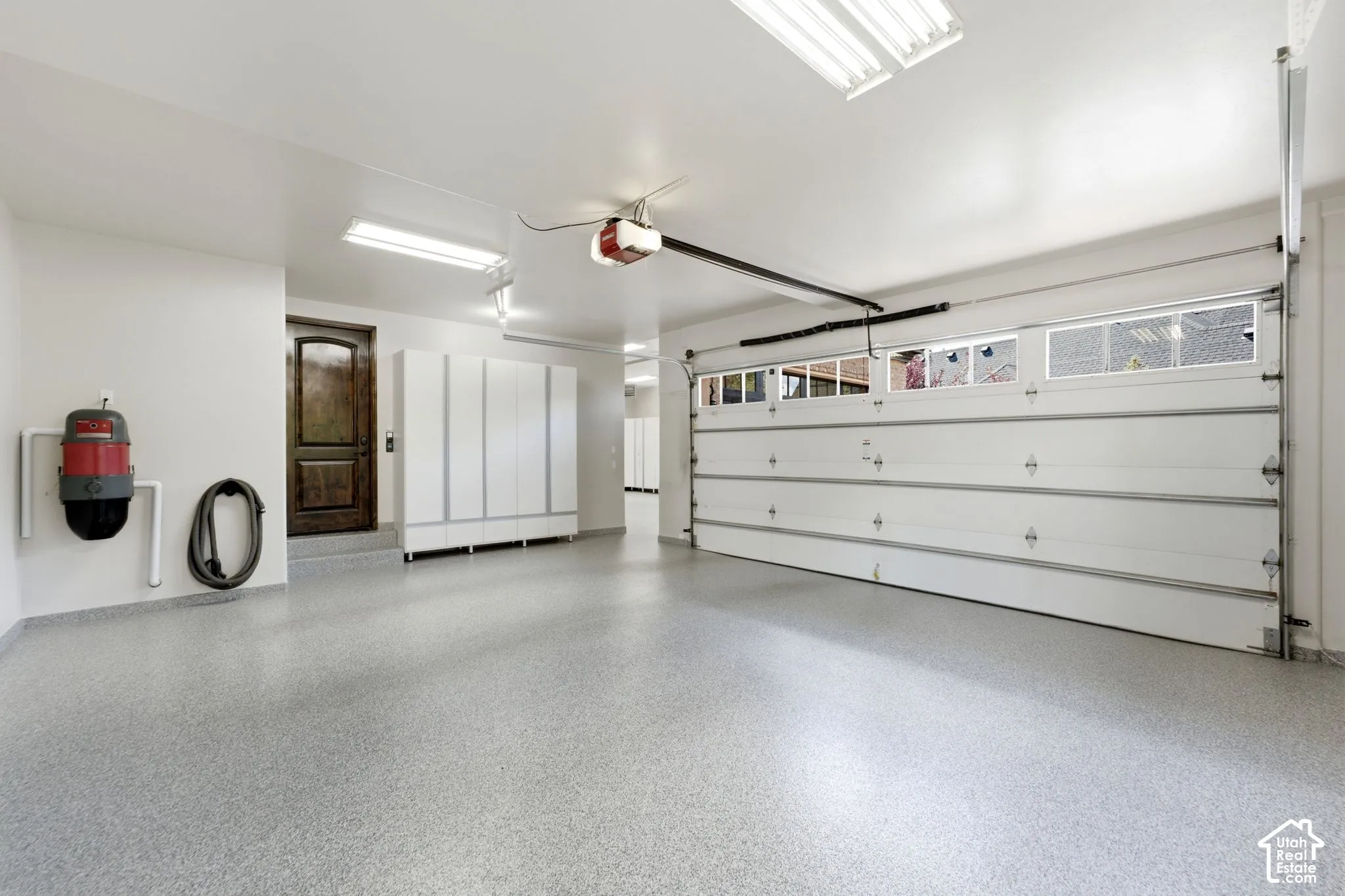 Spacious garage with light gray speckled flooring, white cabinetry, and a dark wood-finish interior door