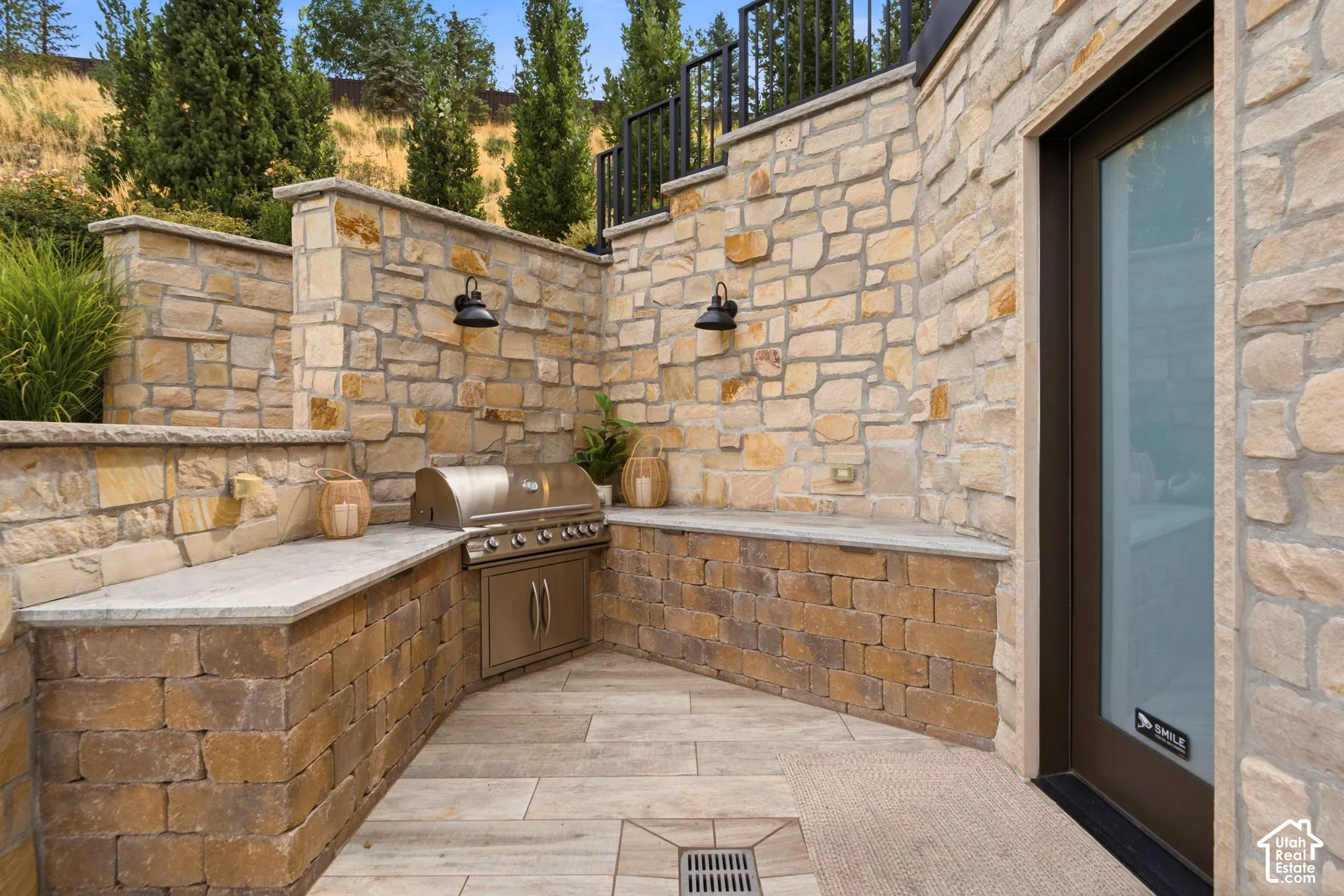 Exterior featuring natural stone walls, a built-in stainless steel grill, light-toned stone countertops, and integrated outdoor lighting fixtures