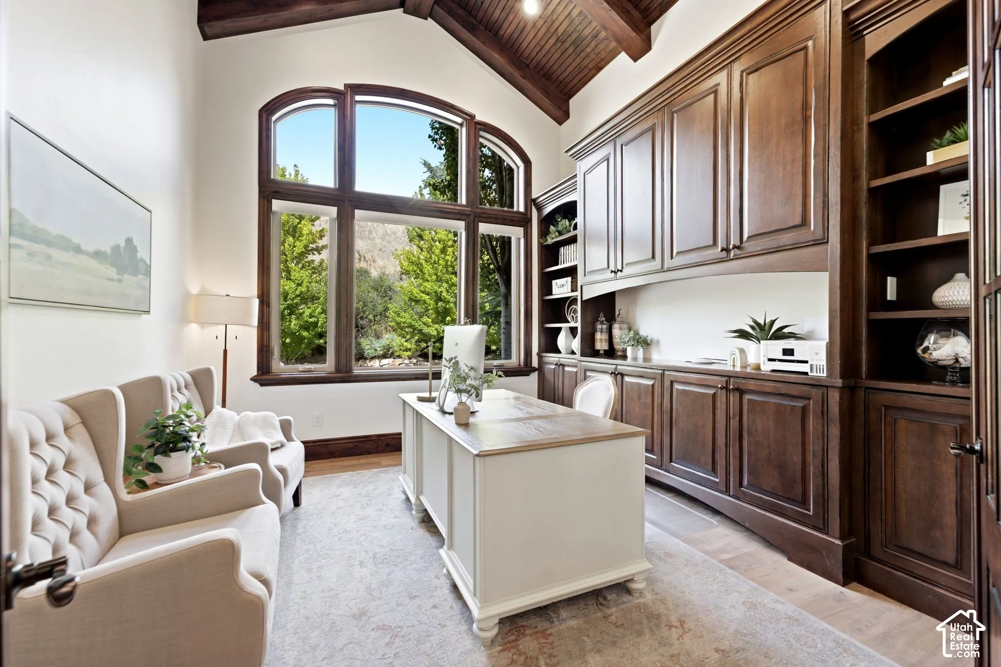 Vaulted wood-paneled ceiling, expansive arched window, built-in dark wood cabinetry, integrated shelving, and light-toned flooring