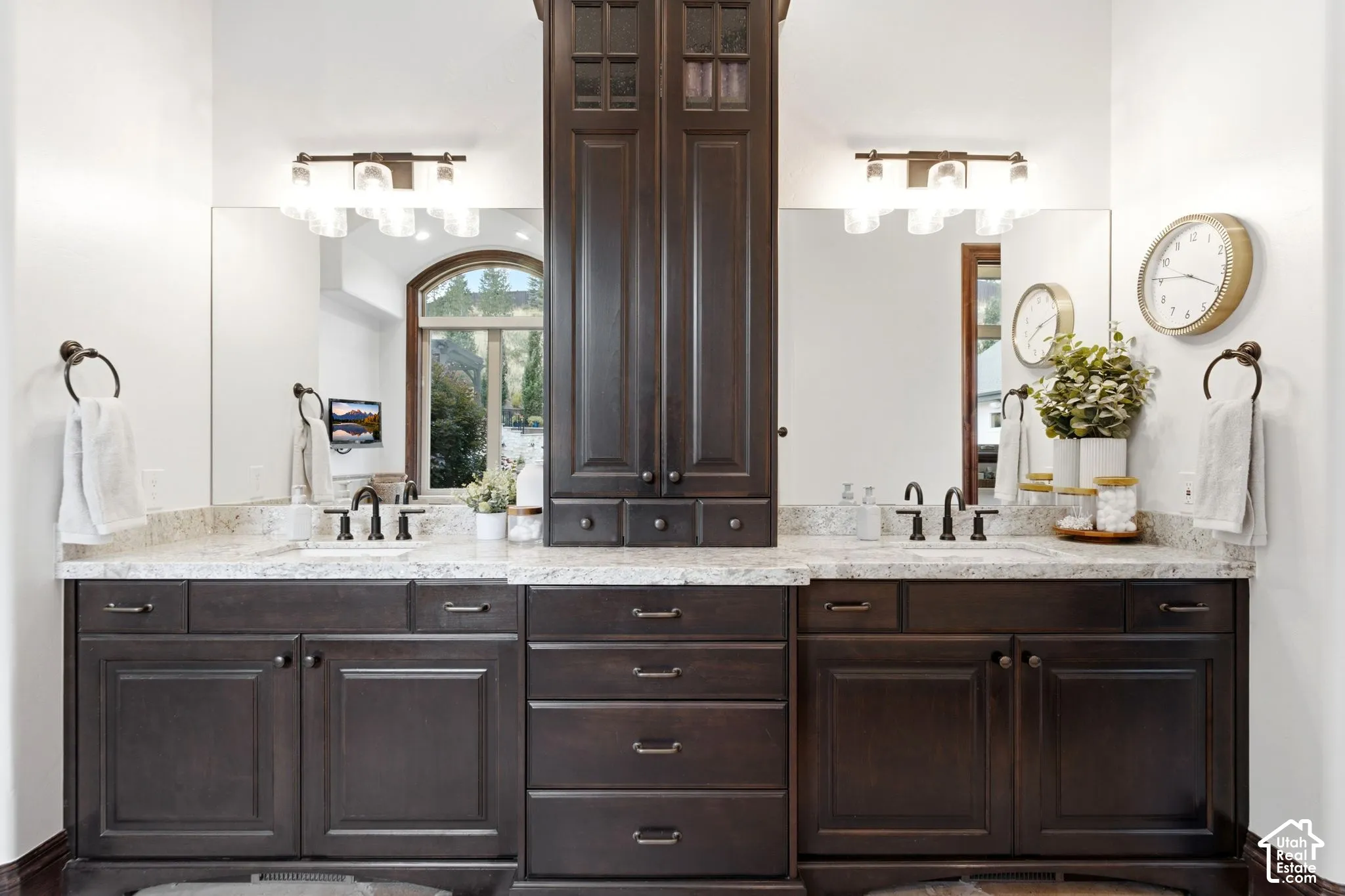 Dual vanity featuring dark wood cabinetry, light-toned countertops, and two wall-mounted light fixtures