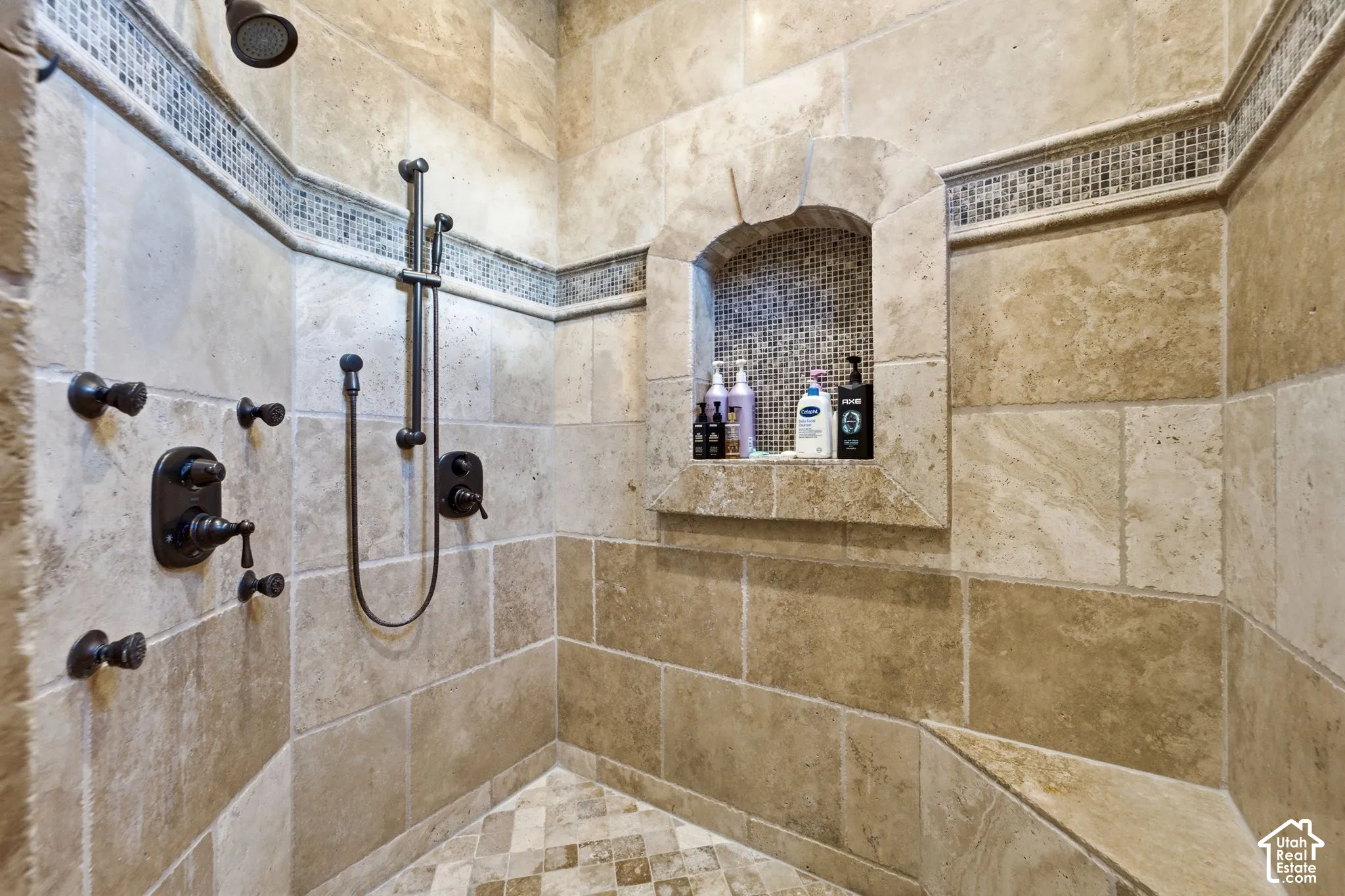 Stone-tiled shower featuring a recessed niche, an integrated bench, and a mosaic tile accent band