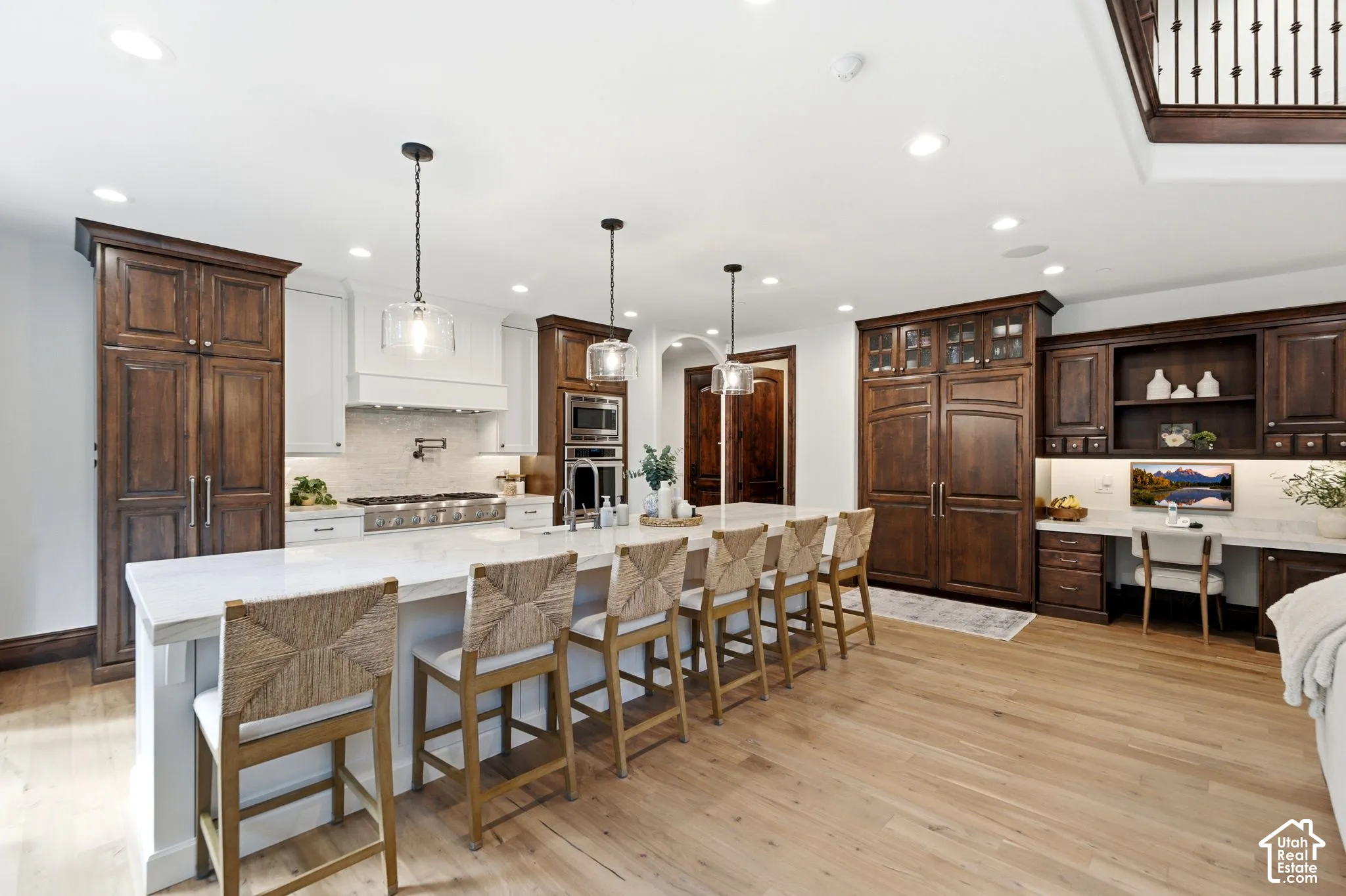 Light wood-finish flooring, a large kitchen island with seating, dark wood cabinetry, a built-in desk area, and recessed lighting