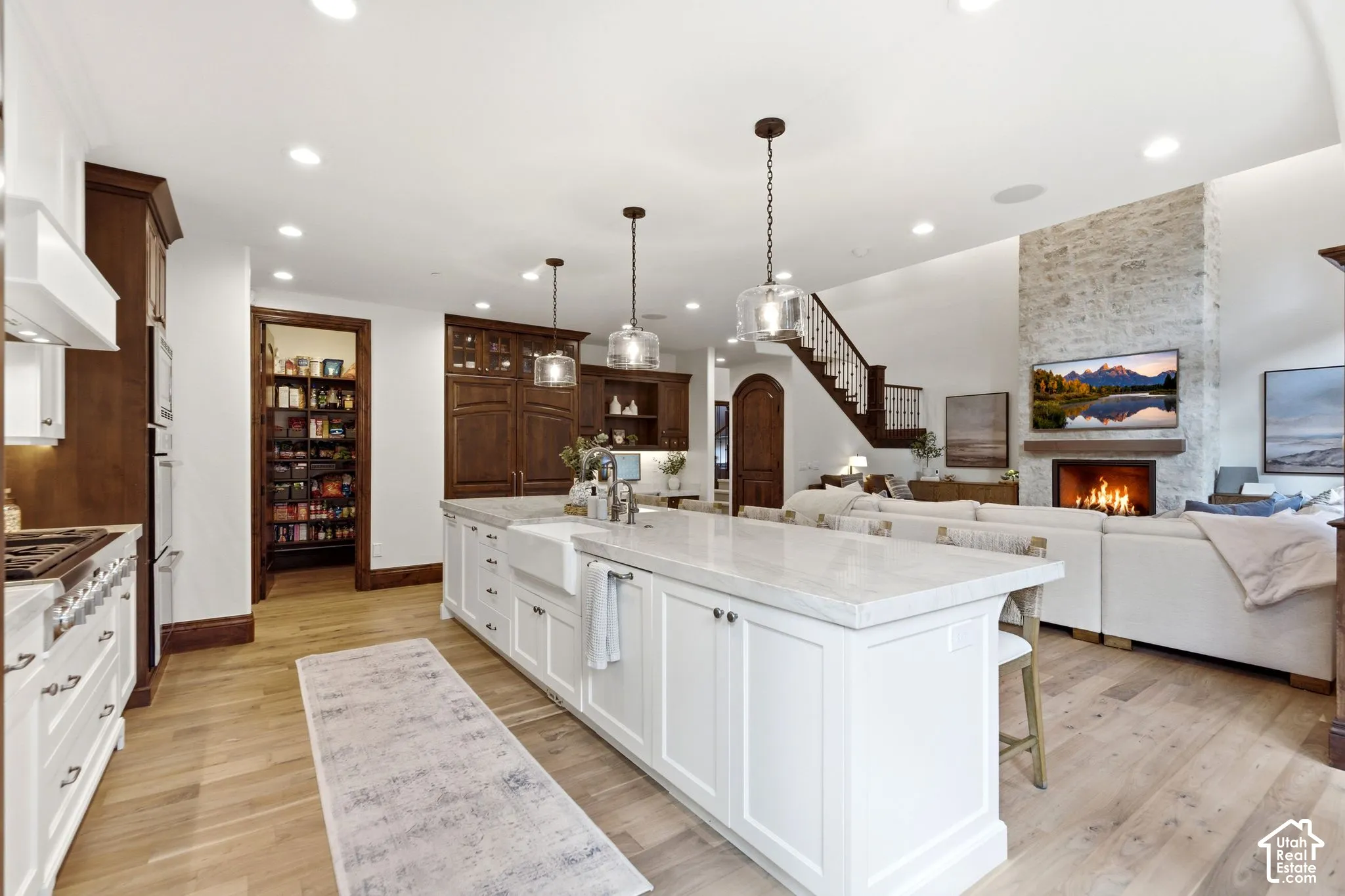 Spacious kitchen featuring a large central island with a farmhouse sink, light wood-finish flooring, and a walk-in pantry