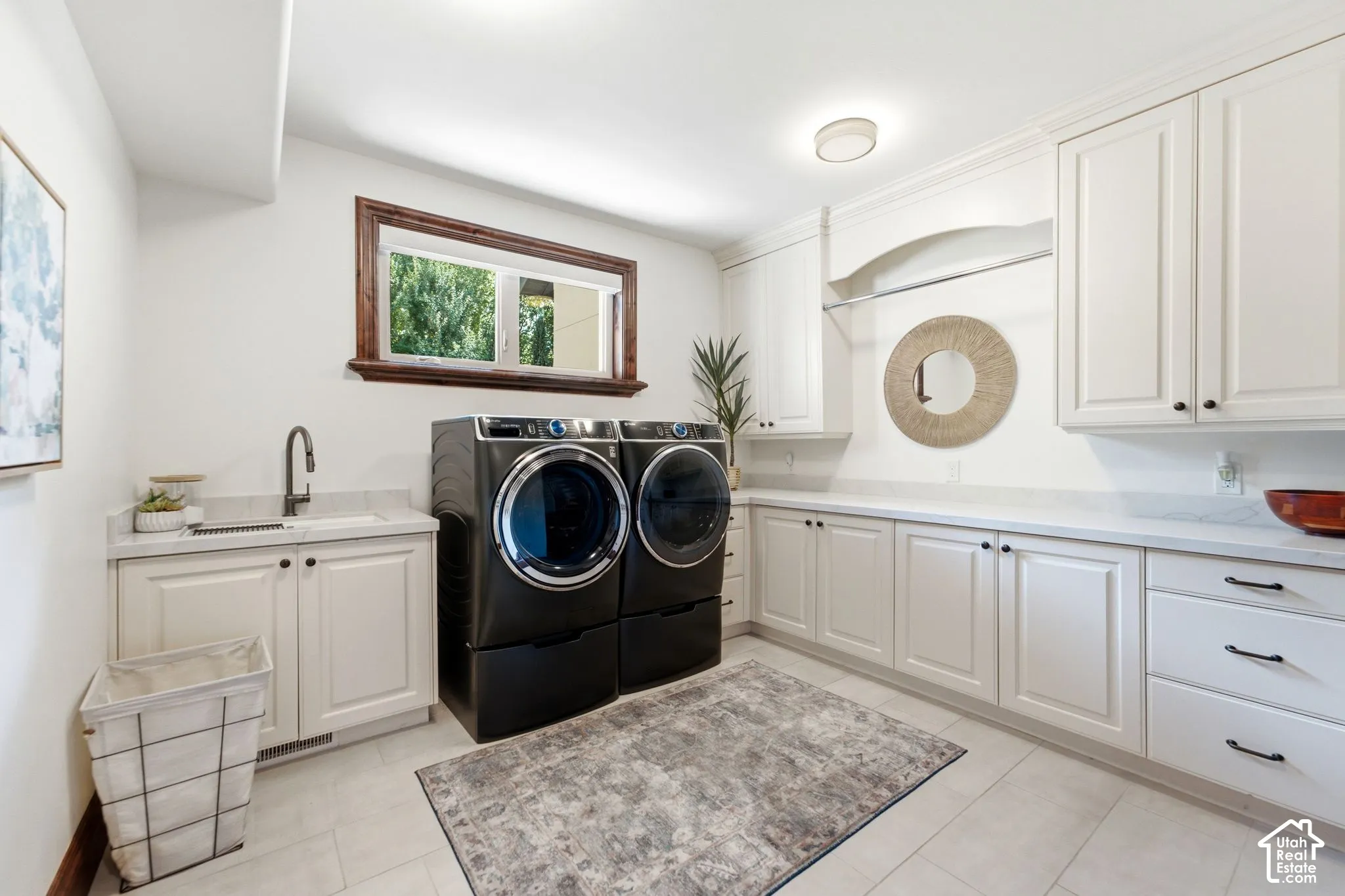 Spacious laundry room with extensive white cabinetry, light-toned countertop surfaces, a utility sink, and wood-framed window