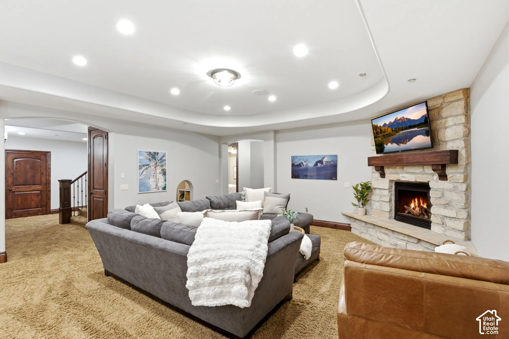 Stone-clad fireplace with wood mantel, recessed ceiling lighting, and arched doorways