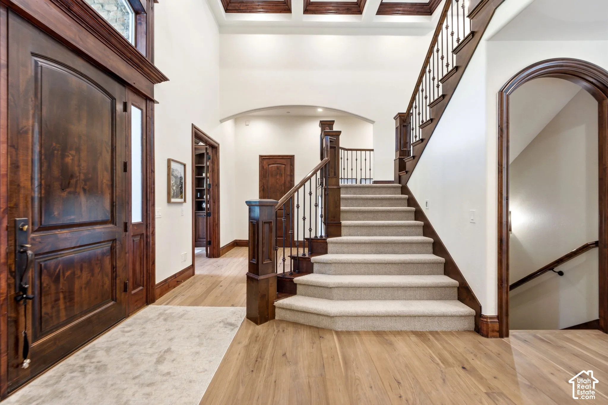 Grand entryway featuring a two-story ceiling, wood-finish flooring, a substantial wood staircase with wrought iron balusters, and a solid wood entry door with an arched transom