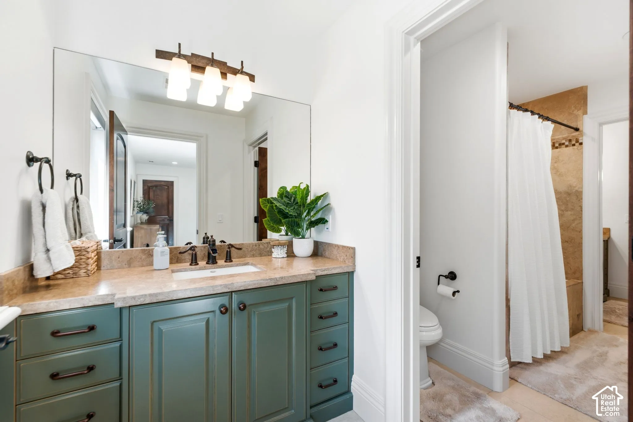 Primary bathroom featuring a dual-sink vanity with wood-finish countertop, teal cabinetry with bronze hardware, large framed mirror, and integrated lighting fixture