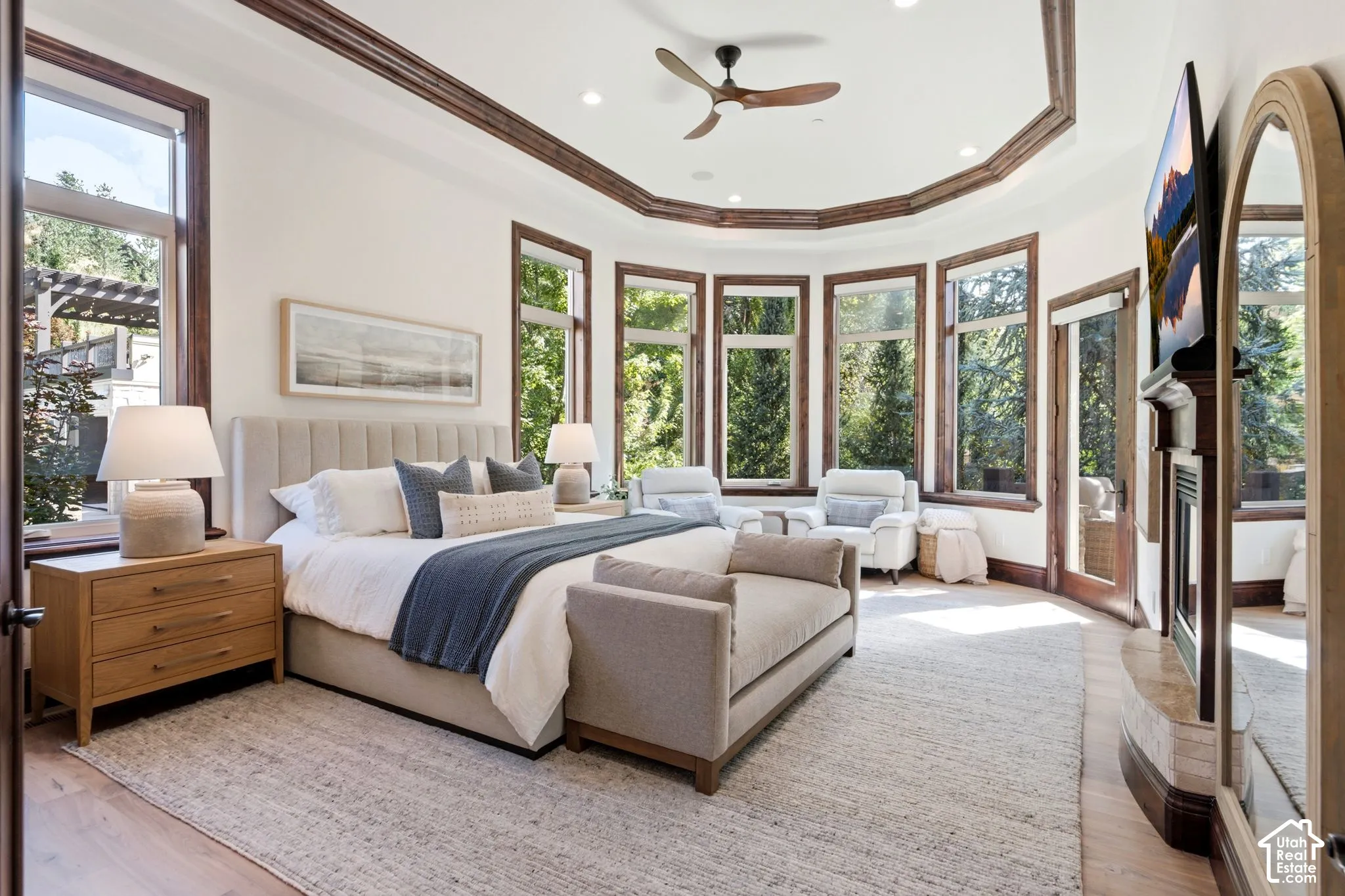 Recessed ceiling with decorative trim, bay window design, wood-finish flooring, built-in fireplace, and ceiling fan