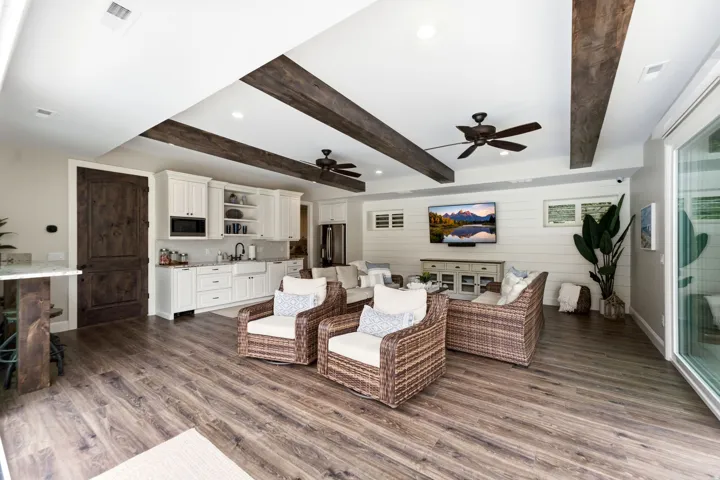 Casita- Open-concept living area with wood-finish flooring, exposed ceiling beams, recessed lighting, and a built-in kitchen area featuring white cabinetry and an apron-front sink