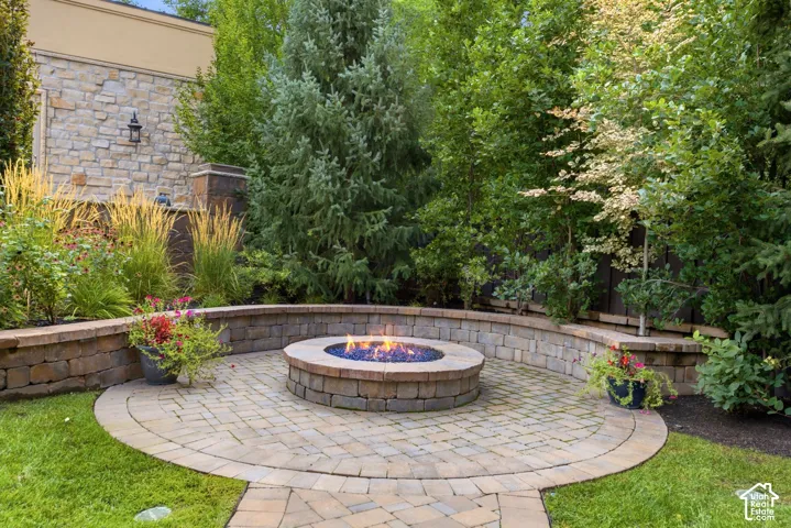 Paver patio featuring a built-in fire pit, surrounded by a stone retaining wall with integrated landscaping