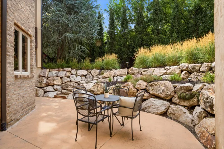 Stone retaining walls with integrated plantings, expansive concrete patio, and a brick exterior facade