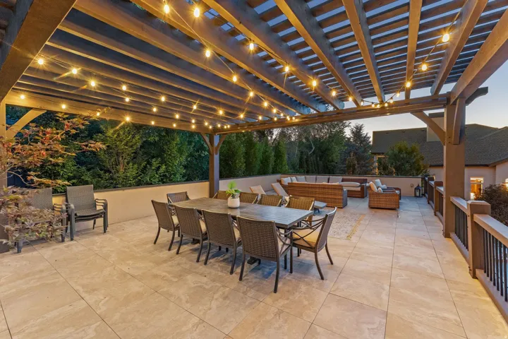 Expansive outdoor patio featuring a wooden pergola, string lighting, and tile flooring