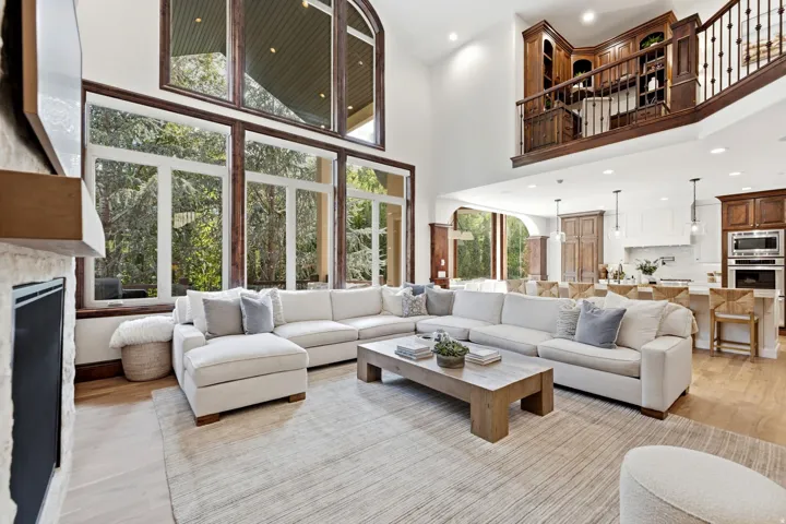Two-story living area with expansive windows, stone-clad fireplace, and a built-in upper-level library